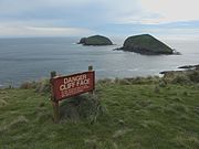 Tanda peringatan tebing di Cape Grim, Tasmania, dengan pulau Doughboy sebagai latar belakangnya.