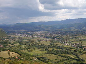 a panoramic photograph of a wide green valley with a small town in the middle distance