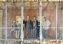 Collage van een foto van migranten op een muur achter een raster.