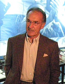 Gino Cappelletti standing in a brown suit.