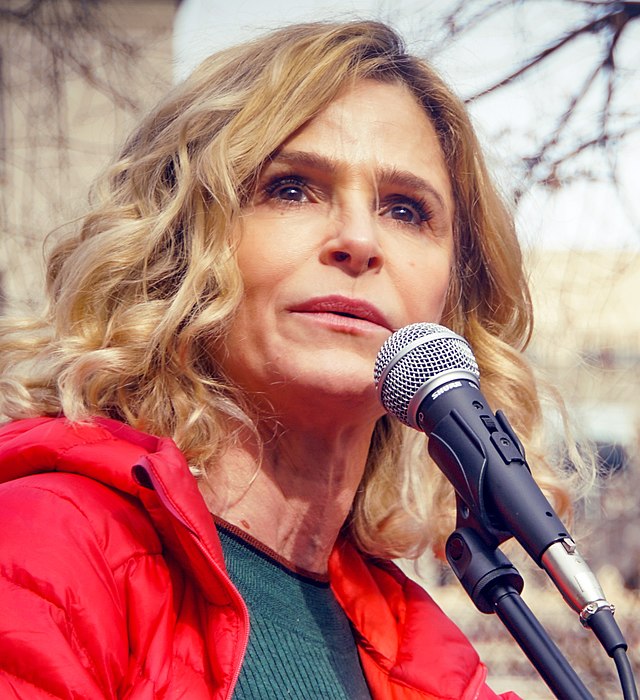 Closeup of a woman's face speaking into a microphone, her eyes are looking out into a crowd