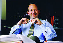 A man wearing a shirt and tie sitting behind a desk