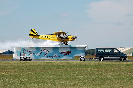 A "clipped-wing" Piper J3C-65 of O'Briens Flying Circus Aerobatic Stunt Team lands on a moving trailer at Cotswold Airport