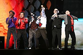 Six men dressed in variously colored clothes performing on a stage.