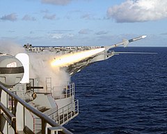 Firing of a missile from USS Roosevelt while at sea, seen from the flight deck. There is a Phalanx cannon on the left, with a white, domed upper section and a black cannon on the lower part.