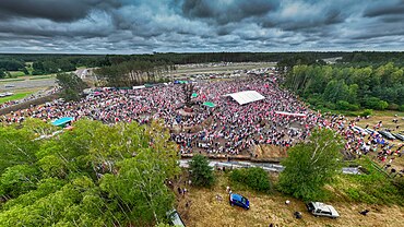 Uroczystość odsłonięcia pomnika "Rzeź Wołyńska" w Domostawie, widoczny tłum ludzi z biało-czerwonymi flagami, otaczający pomnik i polową scenę.