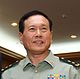 a smiling man with his mouth open and looking rightwards, wearing a light green military uniform with insignia and badges