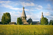 Bâtiment religieux en architecture en bois russe dans un champ par ciel bleu.