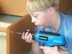 A boy with Down syndrome using cordless drill to assemble a book case.jpg