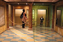 Photograph of two adults standing in an Ames room, apparently with a significant difference in size Ames room forced perspective.jpg