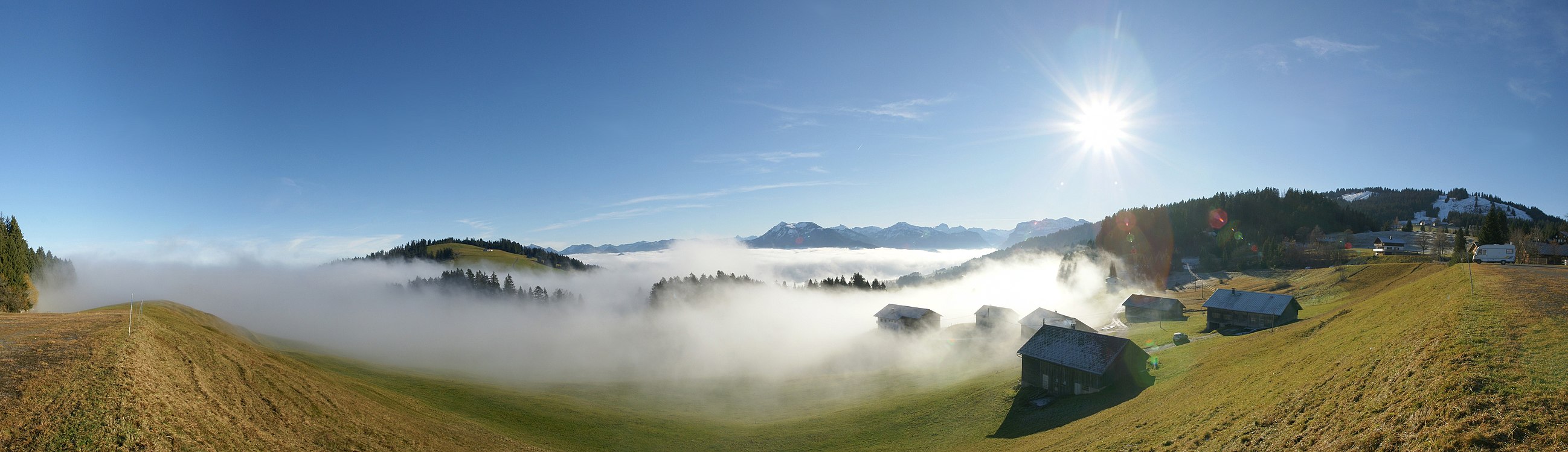 180°-Panorama am Bödele, gelegen zwischen Dornbirn und Schwarzenberg, Vorarlberg, Österreich. Die 2 Bergspitzen in der Bildmitte sind die Winterstaude 1877m und rechts der Hohe Ifen 2230m. Das Bergmassiv unter der Sonne ist die Nordflanke der Kanisfluh. Am rechten Bildrand zu sehen das Skigebiet Bödele mit dem Hochälpelekopf 1464m.