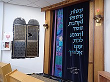 תמונה של פנים בית הכנסת המרכזי בלוד ובו רואים את ארון הקודש וחלון סמוך מזכוכית שנשבר בחלקו עקב זריקת אבנים