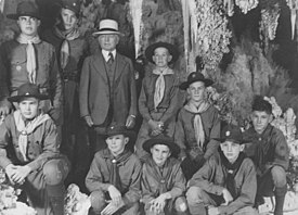 Photograph of Burnham in 1941 celebrating his 80th birthday with several boy scouts. All of them are posing in Carlsbad caverns. The boys are dressed in their boy scout uniforms. Burnham is dressed in a full suit and tie and wearing a white hat.