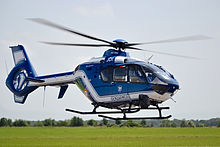 Photo rapprochée d'un hélicoptère aux couleurs blanches et bleues volant à quelques mètres du sol.