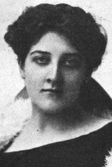 A young white woman with dark hair. She is wearing a dark garment with a white fur stoll or collar visible on one shoulder.