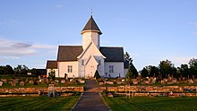 Foto einer weißen Holzkirche, im Vordergrund ein Friedhof