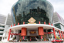 Foto van een groot cilindrisch glazen gebouw, gedecoreerd in de kleuren van China.  Op de voorkant staat de inscriptie "Suria Sabah".