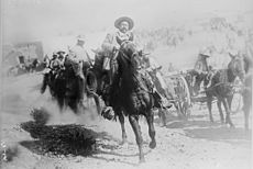 Photographie montrant Pancho Villa, figure célèbre de la révolution mexicaine, sur un cheval un galop, suivi de ses hommes