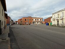 Vista general de la Plaza Mayor del pueblo. Se ve un espacio de carretera amplio con la parada de autobús y casas viejas alrededor de la plaza.