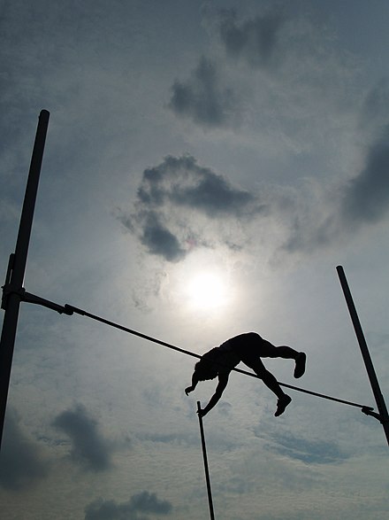 An athlete passes the bar with the aid of a pole.