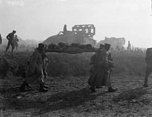 Němečtí vězni nosí zraněného muže, v pozadí tanky Marka V s fašinami, fotografie pořízená 2. října 1918 poblíž Bellicourtu