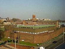 Das Gefängnis in Reading von schräg oben aufgenommen; Gebäudekomplex mit einer umgebenden Backsteinmauer. Im Vordergrund eine Straße mit Autos, im Hintergrund Hochhäuser.
