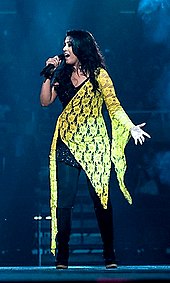 Sunidhi Chauhan actuando en el escenario con un vestido negro y amarillo