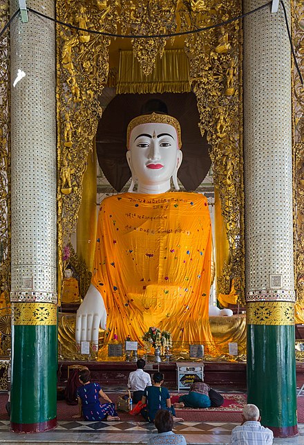 An image of the Buddha at Shwedagon Pagoda is draped with saffron-coloured fabric robes decorated with embroidered lotuses.