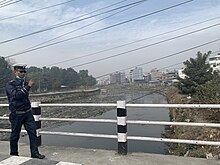 The polluted air visible as smog and piles of trash polluting the Bagmati in Kathmandu, 2023 A bridge over the Bagmati River, Kathmandu District, Nepal (2023).jpg