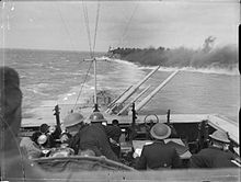 Cleopatra throws out smoke to shield the convoy as Euryalus elevates her forward 5.25 in (133 mm) guns to shell the Italian Fleet during the Second Battle of Sirte, 22 March 1942 HMS Cleopatra smoke.jpg