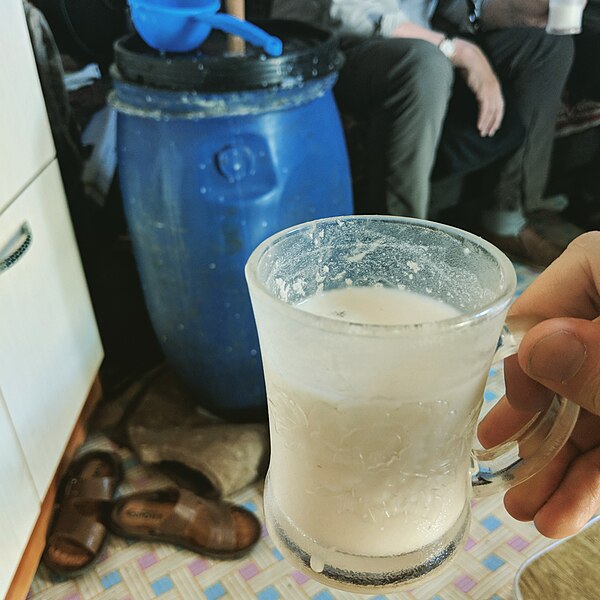 A glass of homemade Mongolian airag, prepared in the blue plastic barrel in the background.