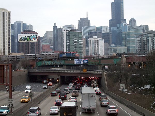 Sign over the Kennedy Expressway, at the north entrance to Hubbard's Cave, encouraging commuters to use Metra trains, such as the one seen here passin