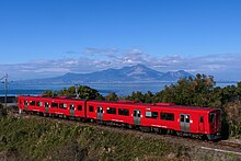 有明海と雲仙岳をバックに三角線の網田 - 赤瀬間を走行するキハ200系