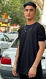 Matin Hassani standing in front of a white Kia Pride in a black t-shirt with a silver chain.