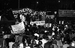 A crowd of people looking at five people standing on a platform in front of a banner that says "Movimento Judío por los Derechos Humanos"