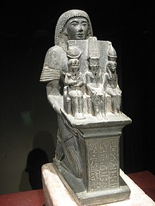 Socha člověka, který sedí a drží tři menší sochy bohů