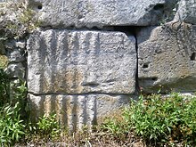 vue d'un grand bloc de pierre partiellement gravé de cannelures, en place dans un mur