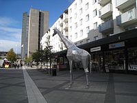 Bilderna visar två olika vinklar av Giraffen i aluminium. Skulpturen donerades till Järfälla kommun 2015 av HSB Norra Stor-Stockholm och står på Riddarplatsen i Jakobsbergs Centrum.
