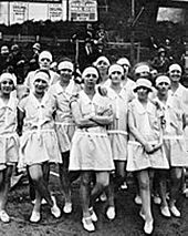 Fotografía en blanco y negro de un grupo de mujeres con vestidos de colores claros, con cintas para el pelo en el pelo
