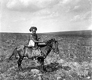 Soembanese man te paard met als bagage een klein speenvarken in een mand van pisangblad
