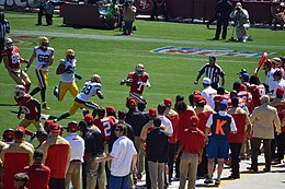 Dans une partie de football américain, de nombreux joueurs sont debout au bord du terrain et regardent l'action en cours.