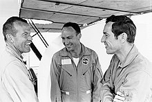 Trois hommes en salopette NASA discutent.