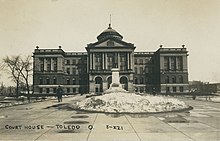 Exterior view of Lucas County Courthouse with man walking and pile of snow.