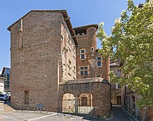 La foto en color muestra una construcción de ladrillos de terracota.  Una fachada cerrada se opone a las ventanas geminadas con marcos de piedra que dan al patio.