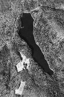 Black and white aerial view of a narrow lake in wooded hills
