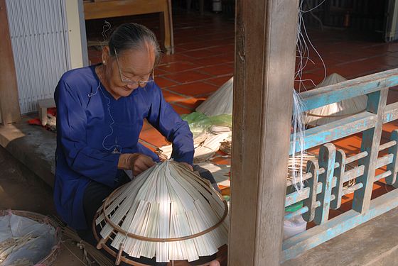 Vietnamese woman in Mekong Delta making traditional conical asian hats from paddy straw.