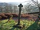 Une queue, simple, croix à bras courts sur une base plate dans un cimetière surplombant un arbre et une vallée verdoyante