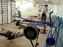 [1] Ein klassischer Fitnessraum, der mit Laufband, Hanteln und Hantelbank sowie einem Rudergerät professionell ausgestattet ist