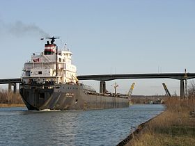 Una nave segue il canale di Welland a St. Catharines, con il ponte levatoio Homer e il cavalcavia per auto di Garden City sullo sfondo.