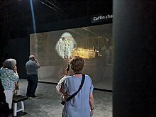 A group of visitors at an edutainment exhibition about Tutankhamun listens to an audio tour synchronized with a projection. Audiotour Edutainment Tut.jpg